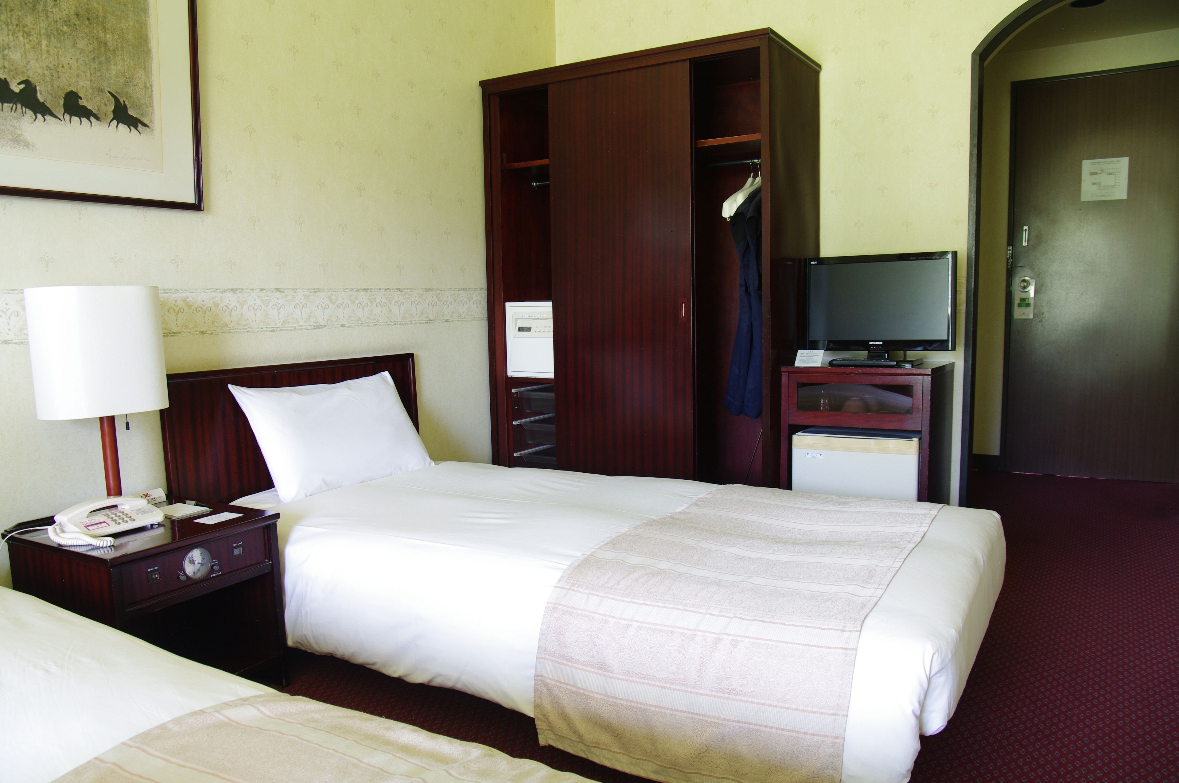 A hotel room with a bed, a nightstand with a lamp, a TV, and a wardrobe.
