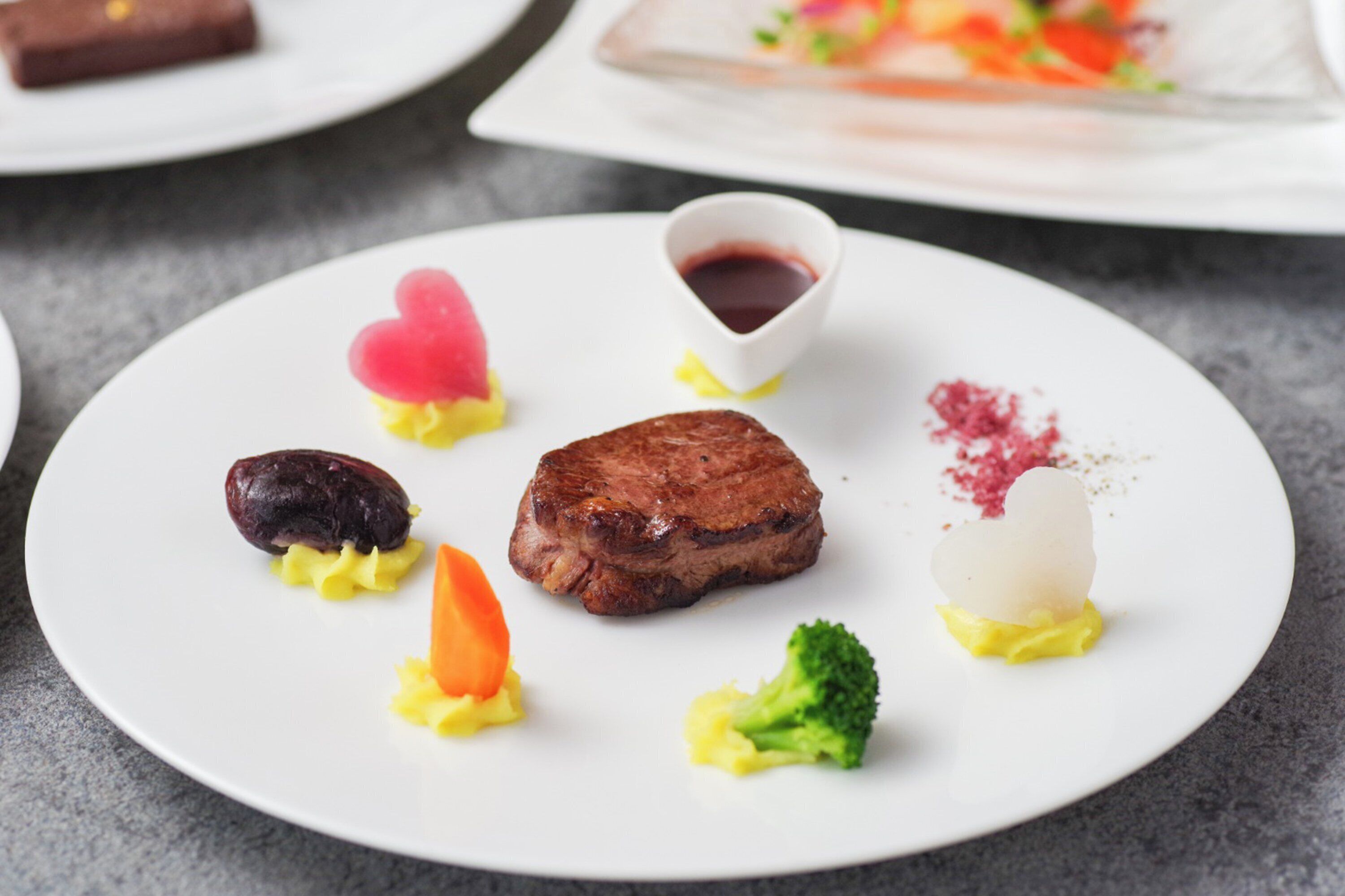 A white plate with a steak, a heart-shaped dessert, and various vegetables.