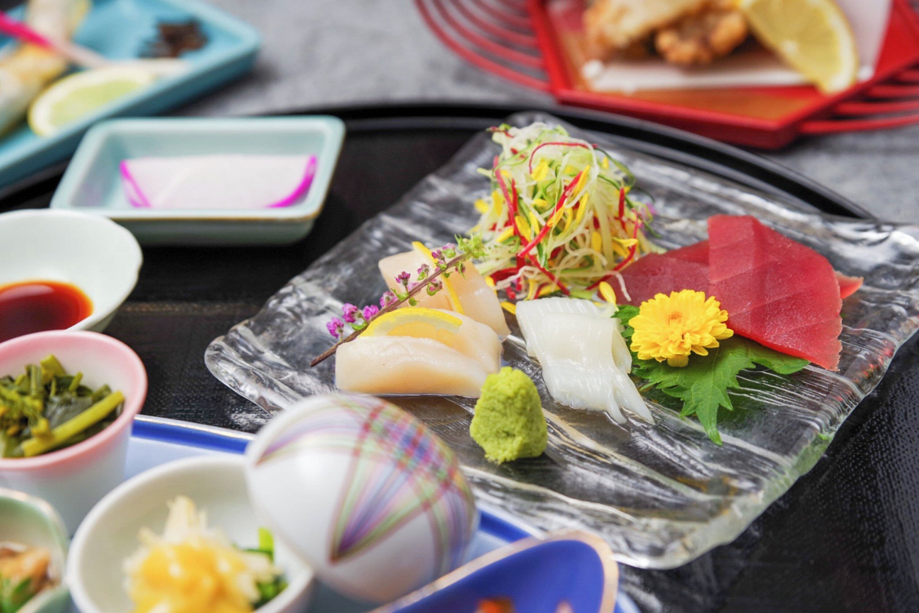 Variedad de platos de sushi sobre un plato de vidrio, acompañados de recipientes pequeños con salsas y verduras encurtidas.