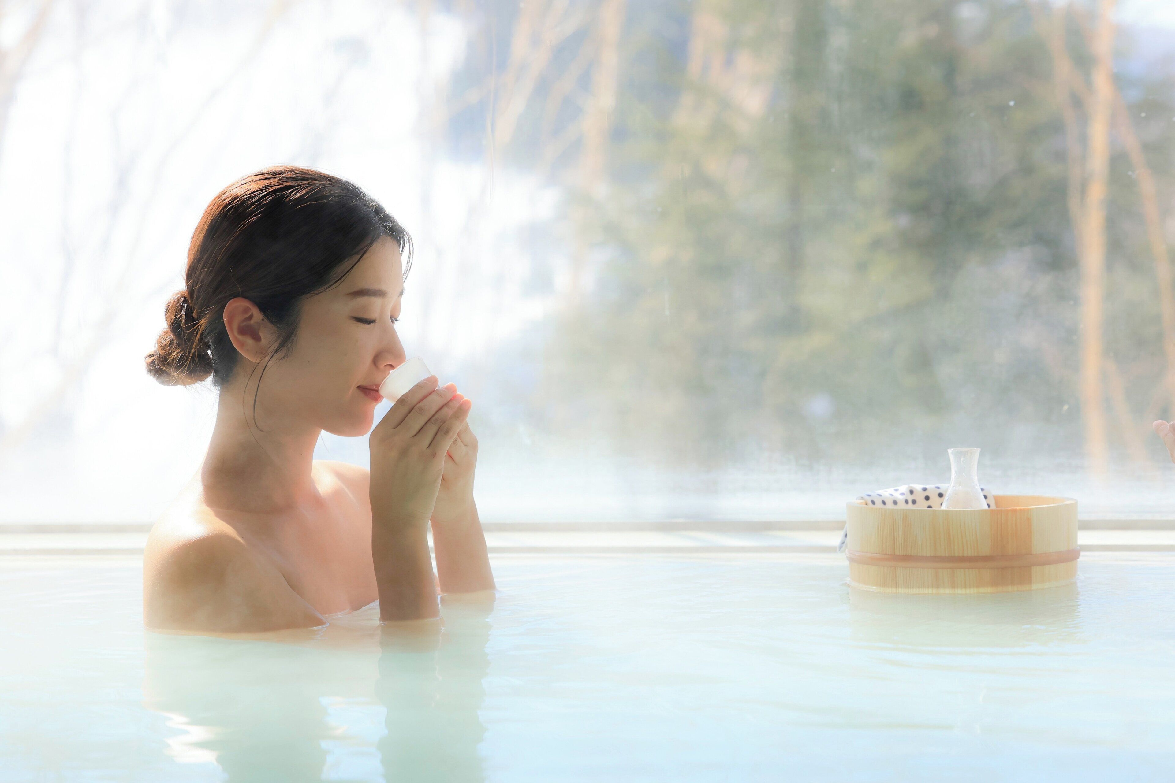 A person in a hot spring with a wooden container on the edge.