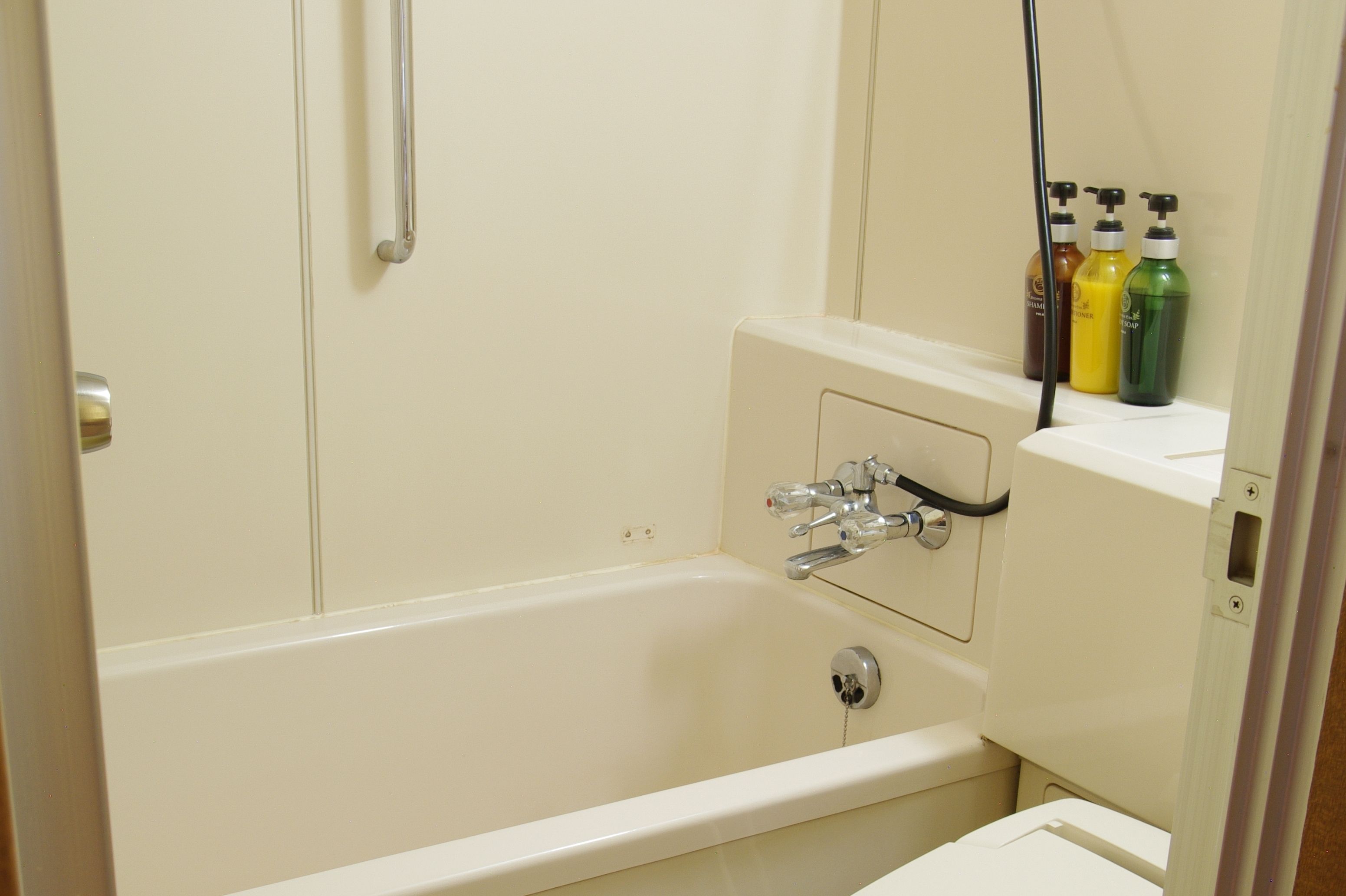 A bathroom with a bathtub, a shower, and a toilet. There are three bottles of shampoo on the wall.
