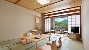 A traditional Japanese room with tatami flooring, a low table with cushions, a television, and a view of a mountainous landscape. - Manza Prince Hotel (Tsumagoi)