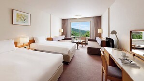 A hotel room with two beds, a desk, a chair, a small table, and a window with a view of greenery. - Manza Prince Hotel (Tsumagoi)