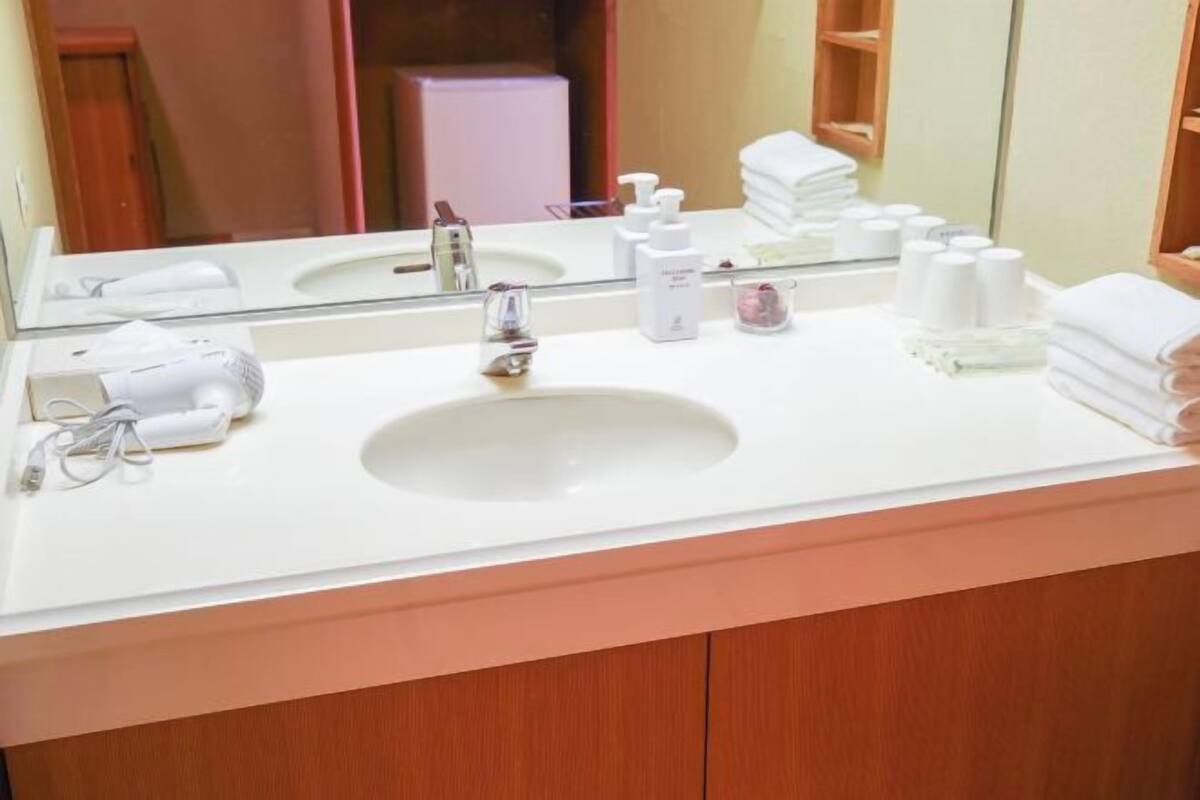 Casa de banho de hotel com uma pia branca, um espelho e produtos de higiene na bancada.