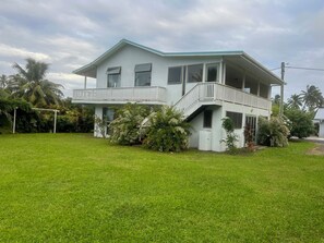 A two-story house with a balcony, surrounded by lush greenery and palm trees. - Raina Holiday Accommodation (Rarotonga)
