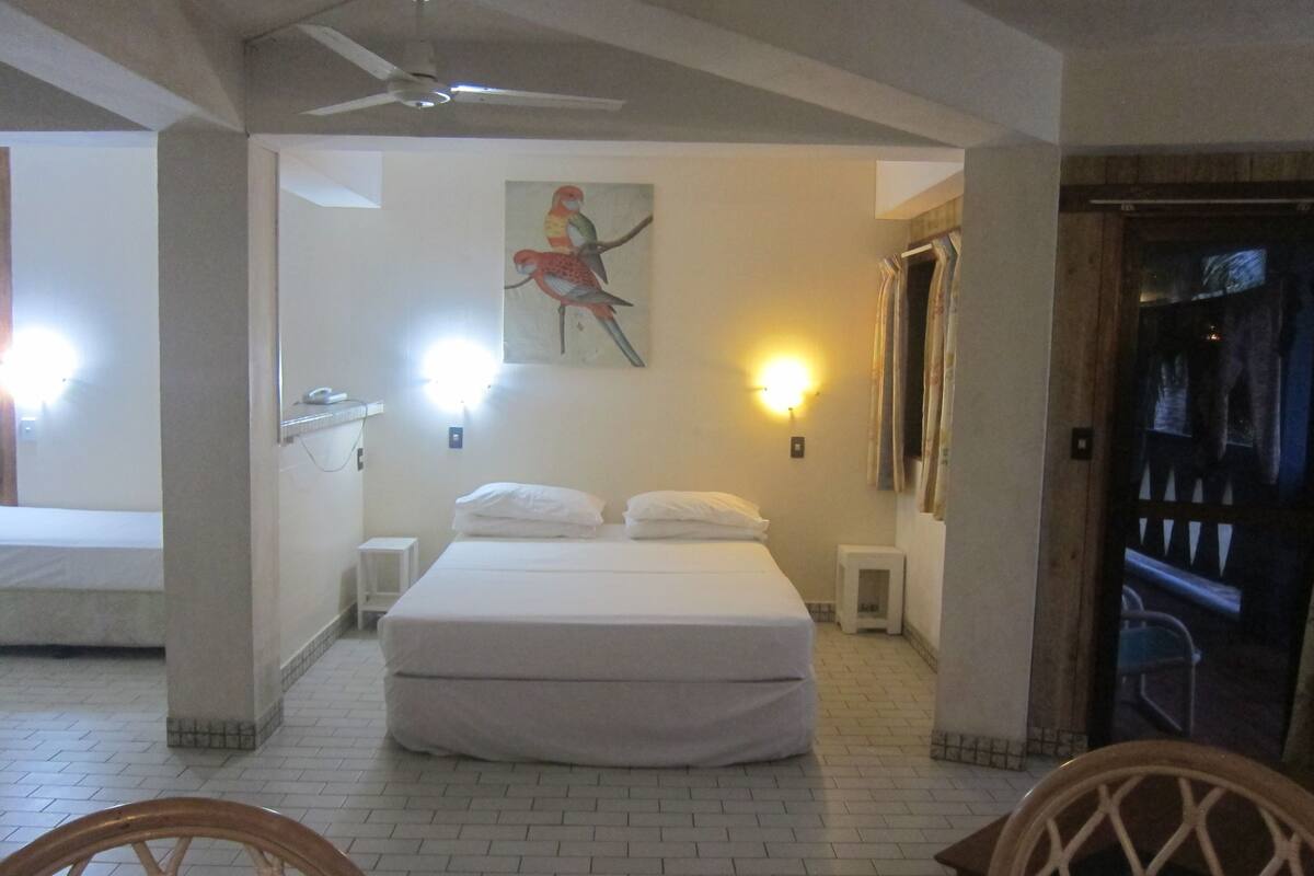 A hotel room with a bed, a ceiling fan, a painting of a bird, and a night light.