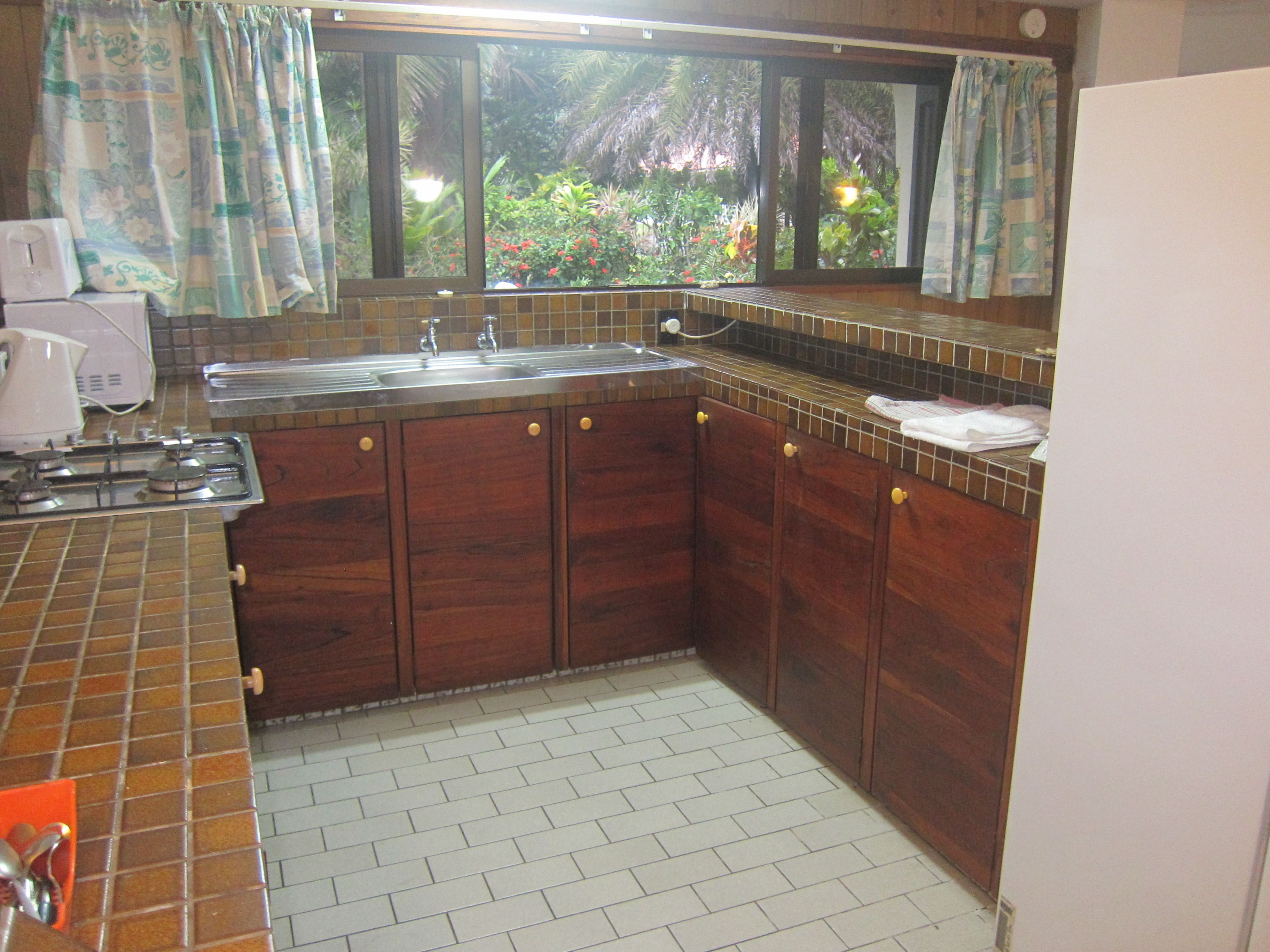Une cuisine avec des meubles de rangement en bois, une cuisinière à gaz, un évier et une fenêtre donnant sur un jardin.