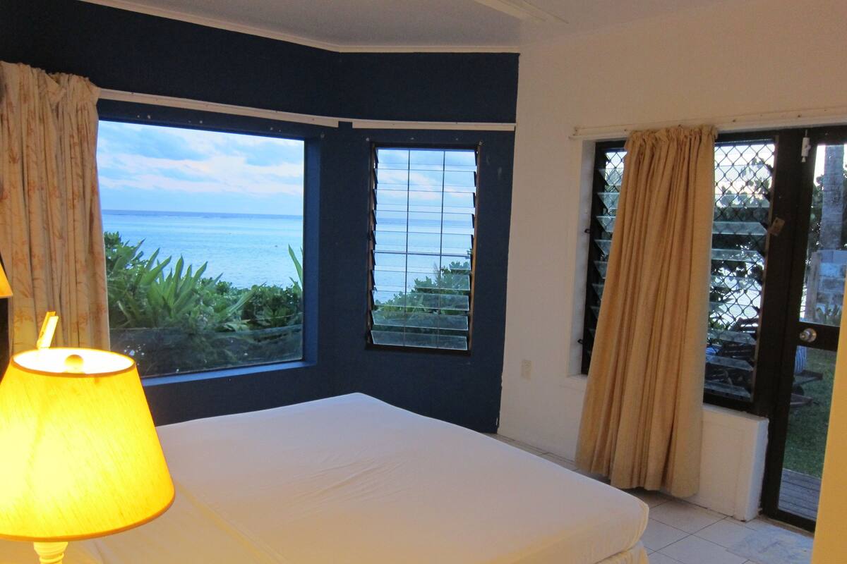 A bedroom with a bed, a window with a view of the sea, and a door leading outside.