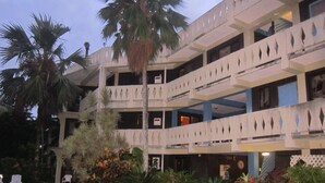 Un edificio a più piani con balconi, circondato da piante in vaso e palme.