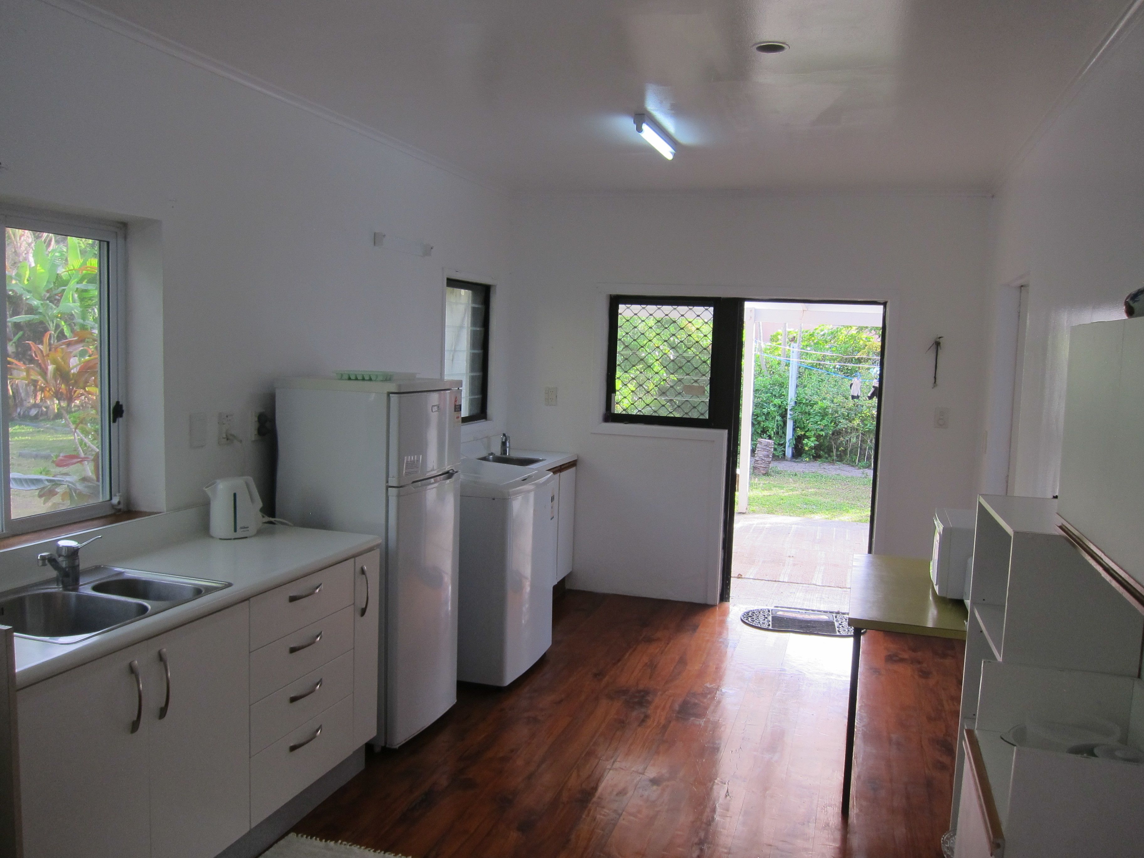 A compact kitchen with white cabinets, a refrigerator, a sink, and a window overlooking a garden.