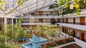 A multi-level atrium with a glass ceiling, indoor plants, seating areas, and a decorative blue water feature. - Muthu Oura Praia Hotel (Albufeira)