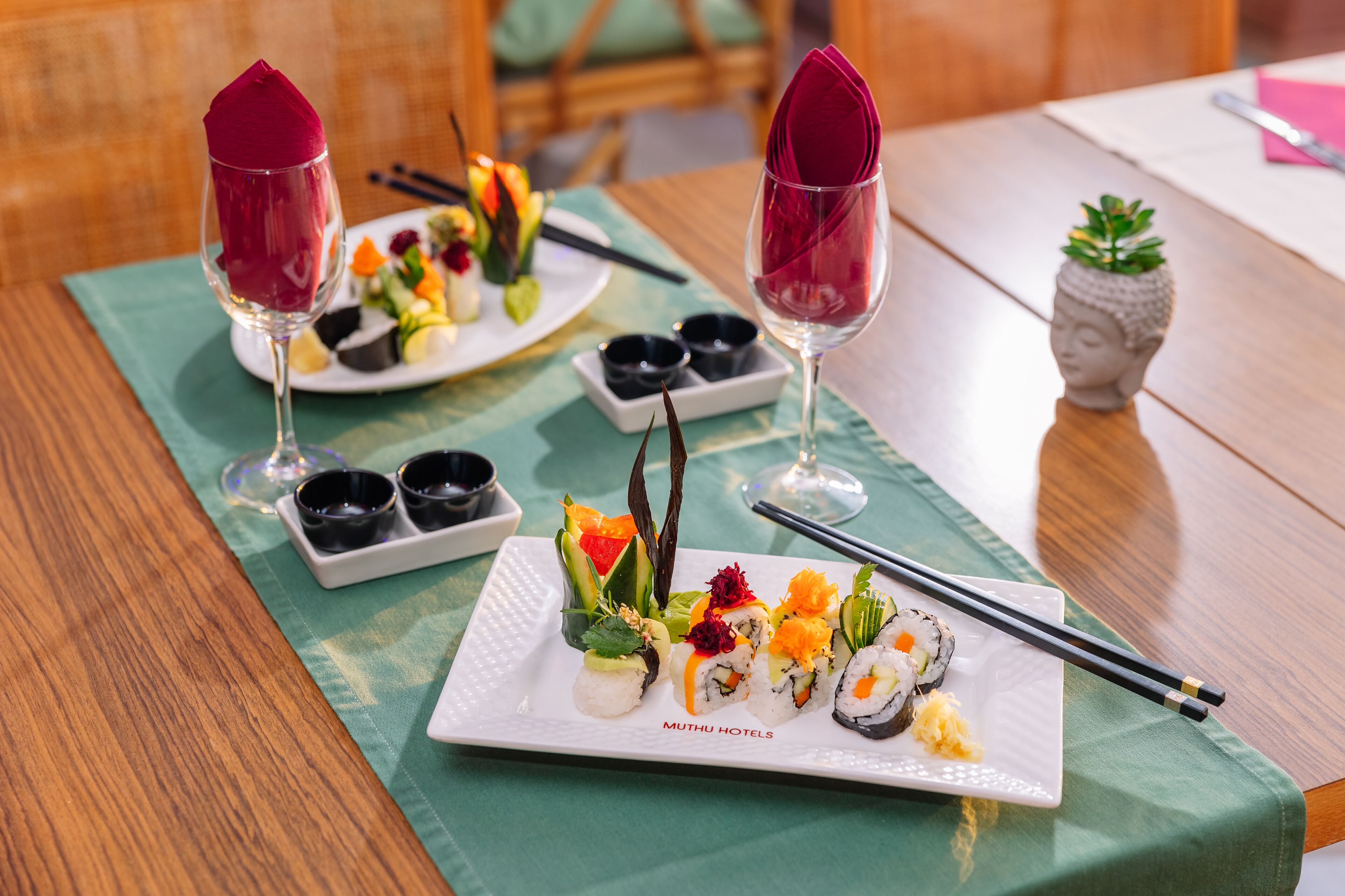A dining table with plates of sushi, two glasses with red napkins, and chopsticks.