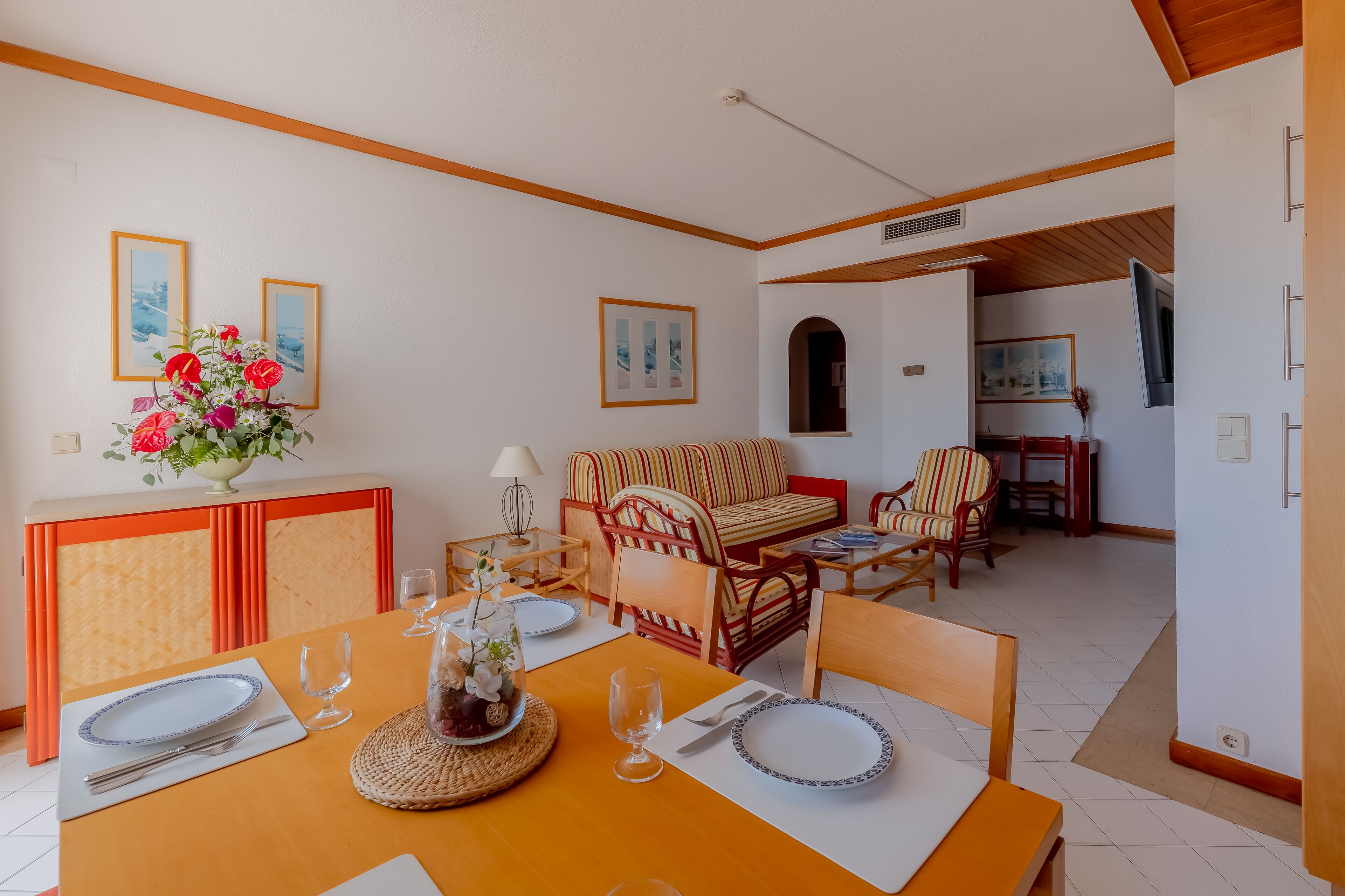 A dining area with a table set for two, a sofa, and a TV in the background.