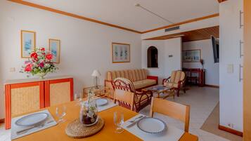 A dining area with a table set for two, a sofa, and a TV in the background.