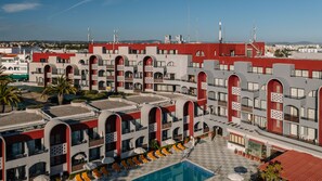 A hotel with multiple floors, outdoor swimming pool, and a view of the surrounding cityscape.
