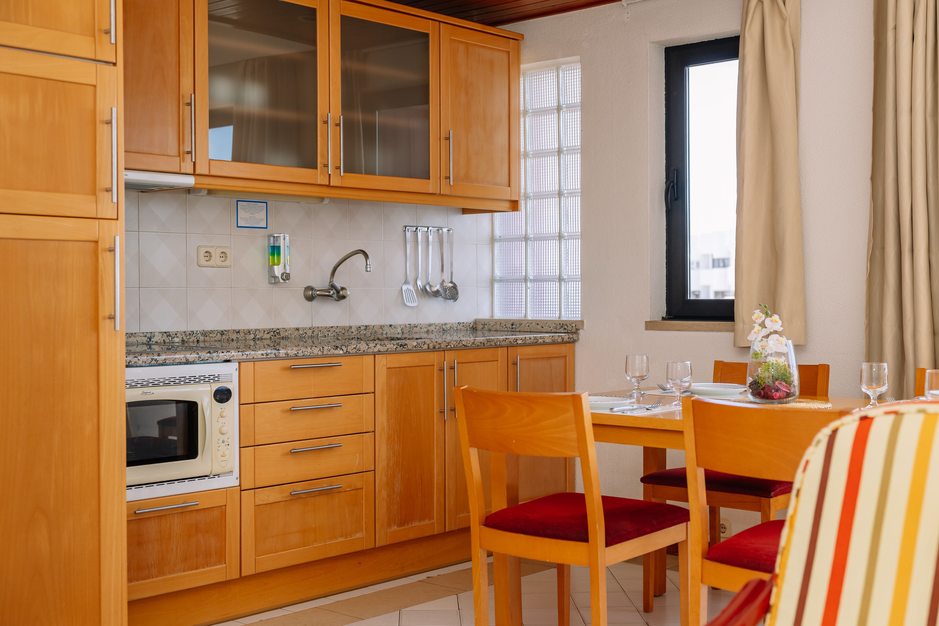 A kitchen with wooden cabinets, a built-in microwave, a sink, and a dining area with a table set for two.