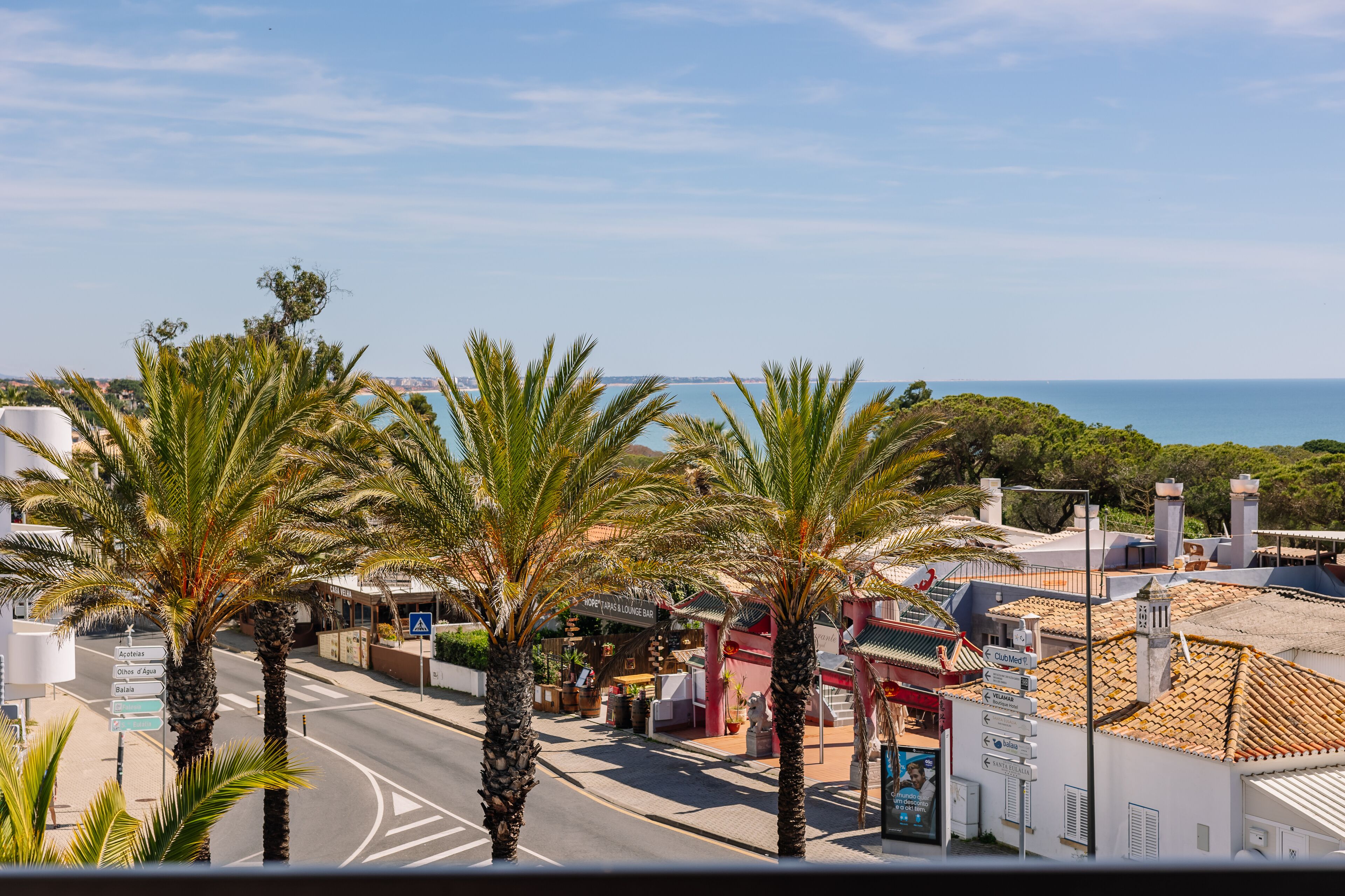 A coastal street with palm trees, a bar, and buildings with traditional architecture.