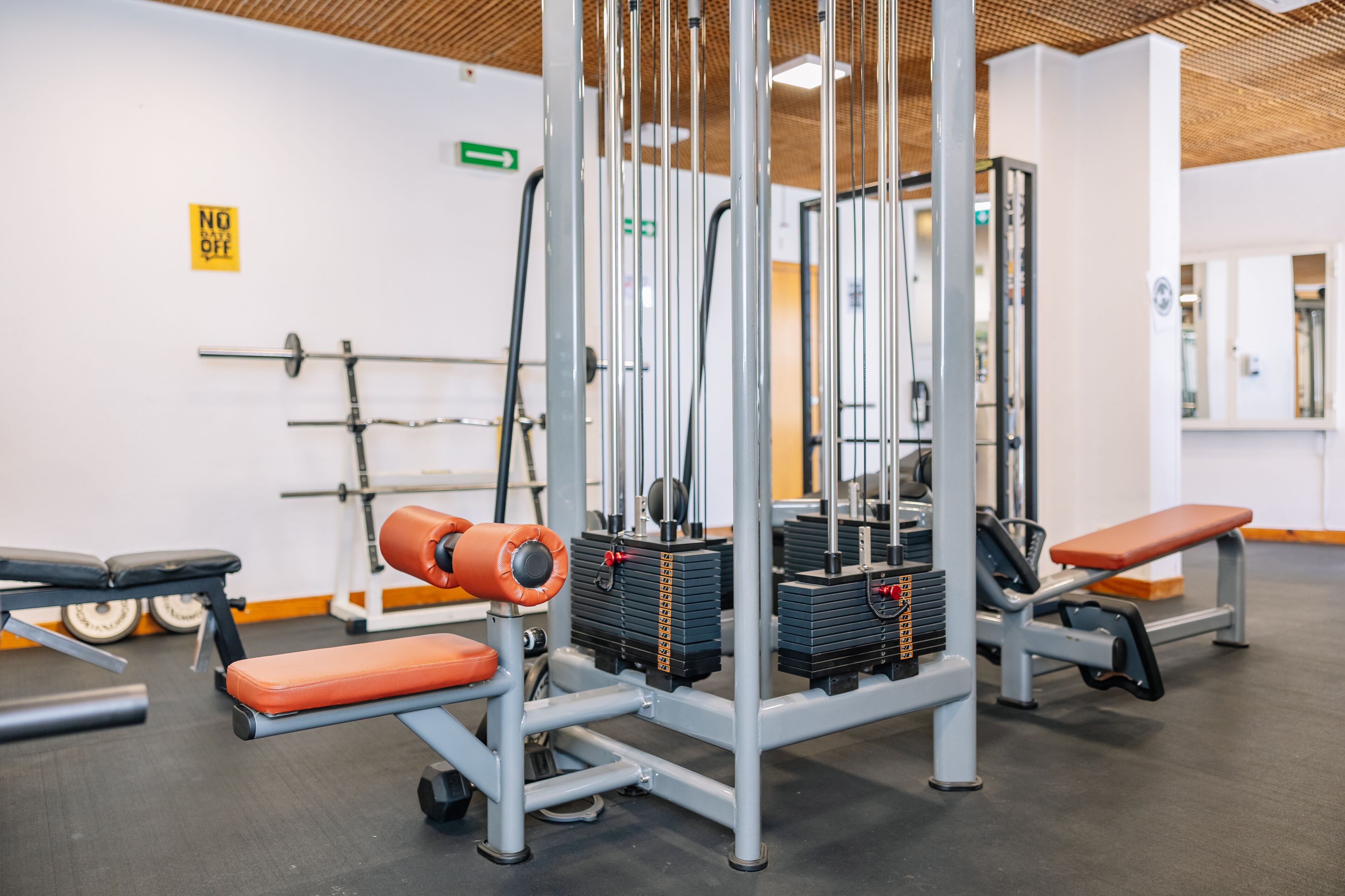 Un gimnasio con equipo de levantamiento de pesas, bancos y un espejo grande.