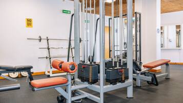 Un gimnasio con equipo de levantamiento de pesas, bancos y un espejo grande.