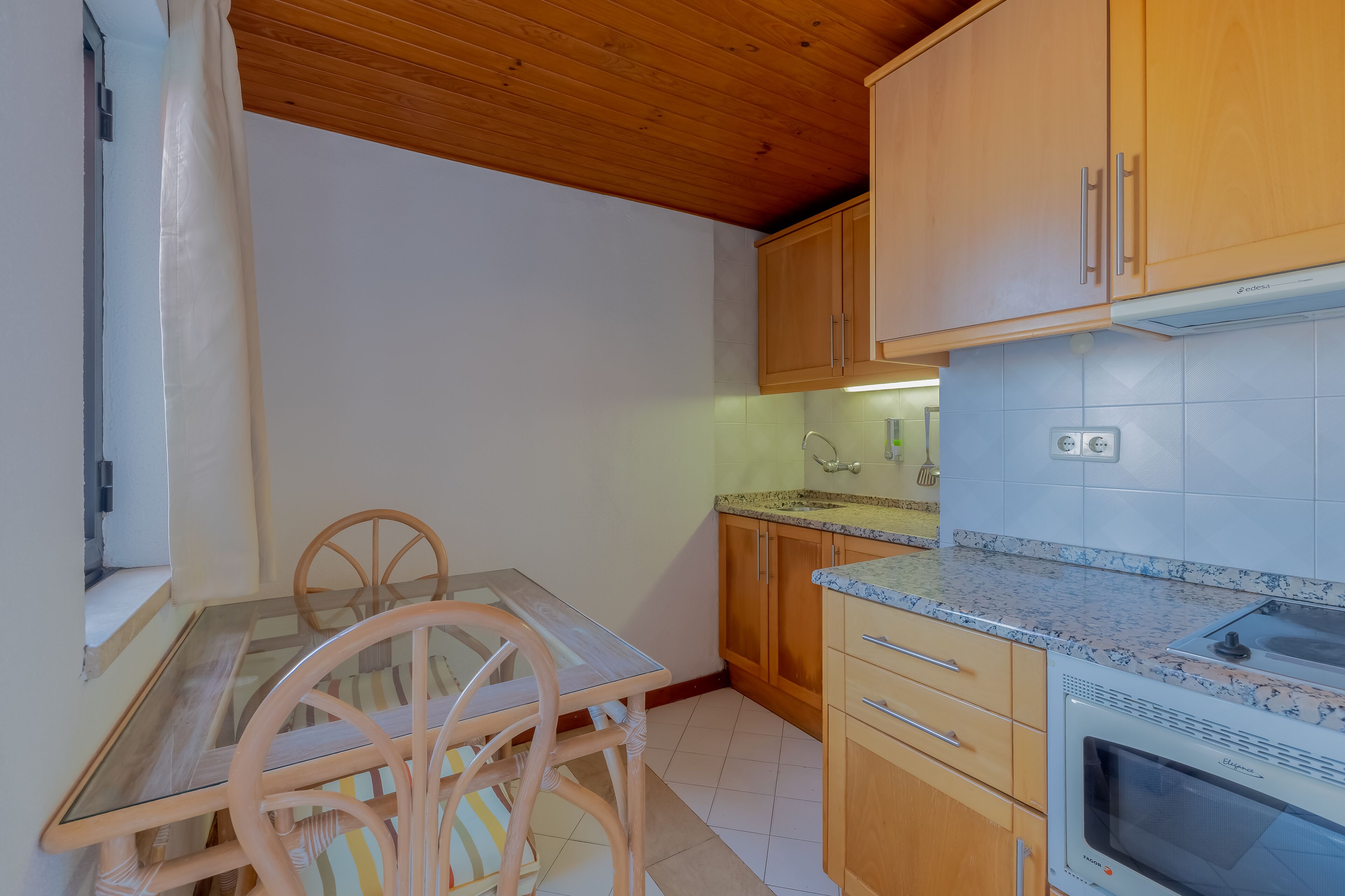 Una cocina con armarios de madera, una mesa de vidrio y un horno empotrado.