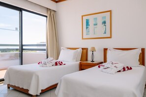 A hotel room with two beds, a large window, and a painting on the wall.