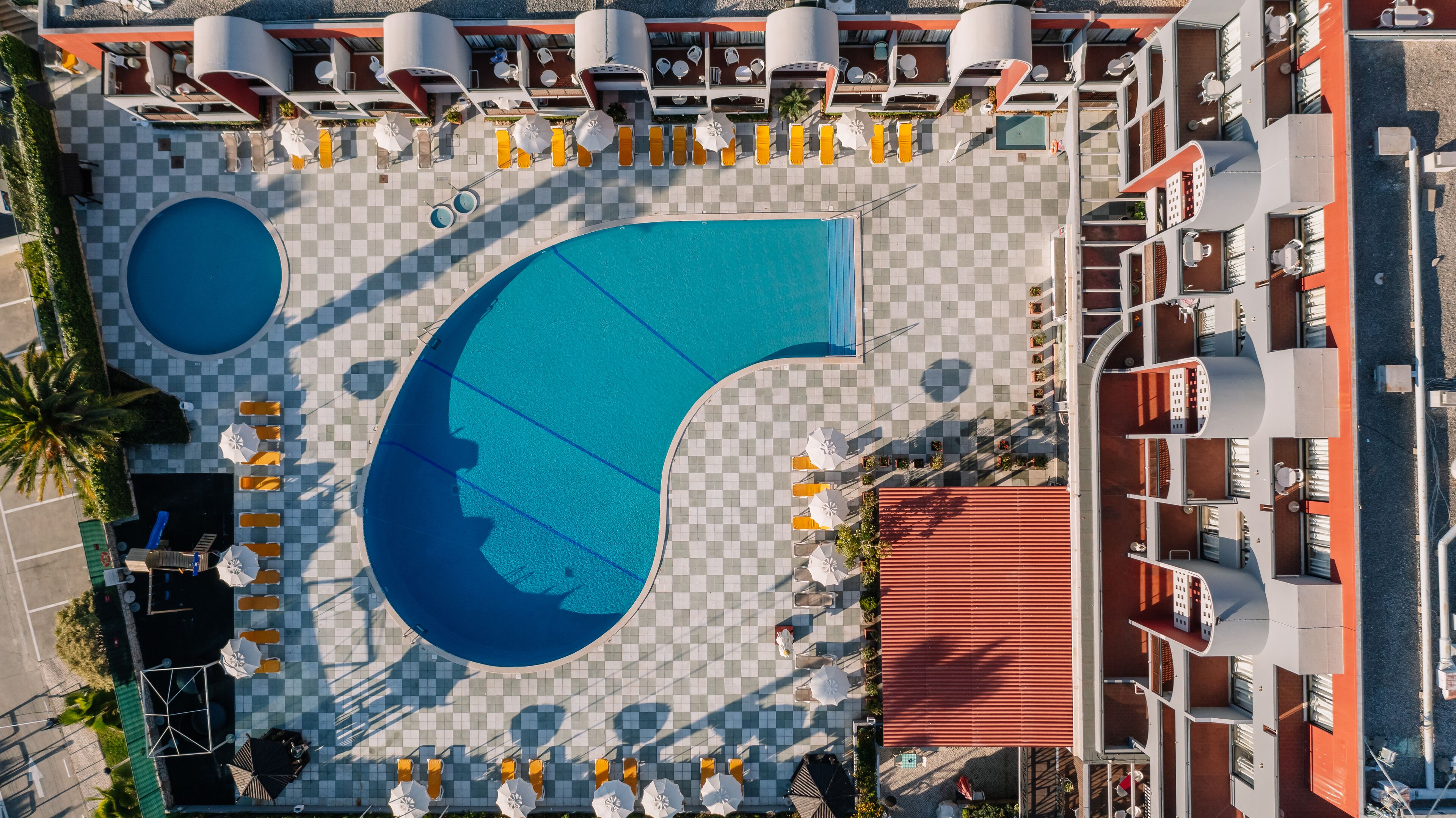 An aerial view of a hotel with a large pool, sun loungers, and a checkered floor.