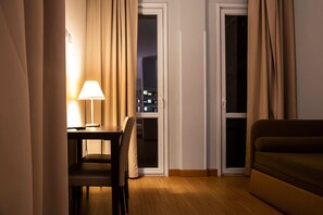 Ein Hotelzimmer mit Esstisch, einem Stuhl, einer Couch und zwei mit Vorhängen versehenen Fenstern.