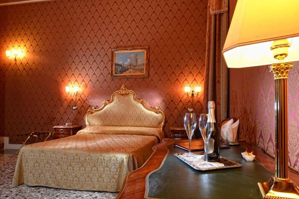 Une chambre d’hôtel avec un grand lit, une table de chevet en bois sur laquelle se trouve un plateau, et des appliques murales.