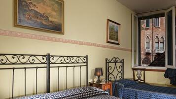 A room with two beds, a painting, and a window with a view of a building.