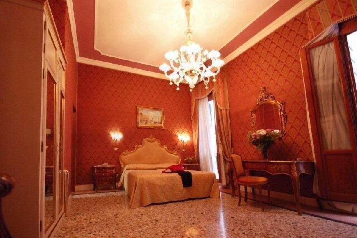 Une chambre d’hôtel avec un grand lit, un lustre, un bureau avec une chaise et un miroir.
