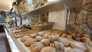 Een buffet met diverse gebakjes en brood, waaronder croissants en bladerdeeg, gepresenteerd op een toonbank met een achtergrond van een stenen muur.