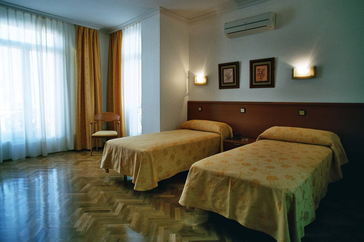 A hotel room with two beds, a chair, and a window with curtains.