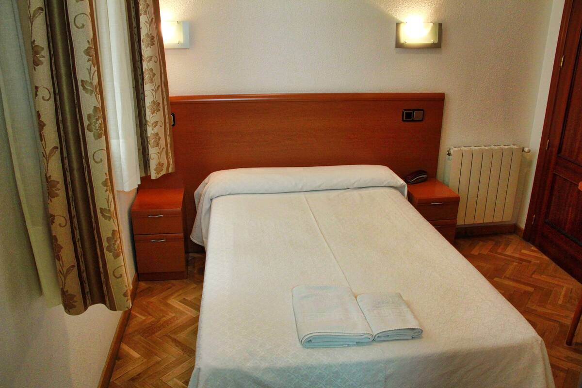 A single bed with a wooden headboard, a nightstand, a bedside table, and a radiator.