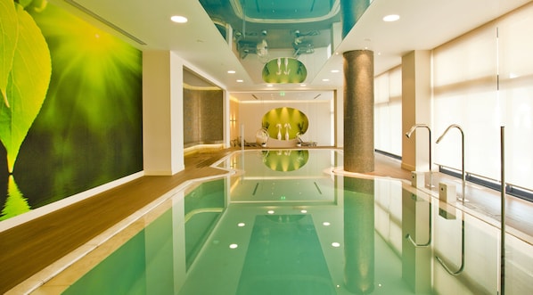 A modern indoor swimming pool with a green-tinted water surface, a wooden floor, and a large mural on the left wall.