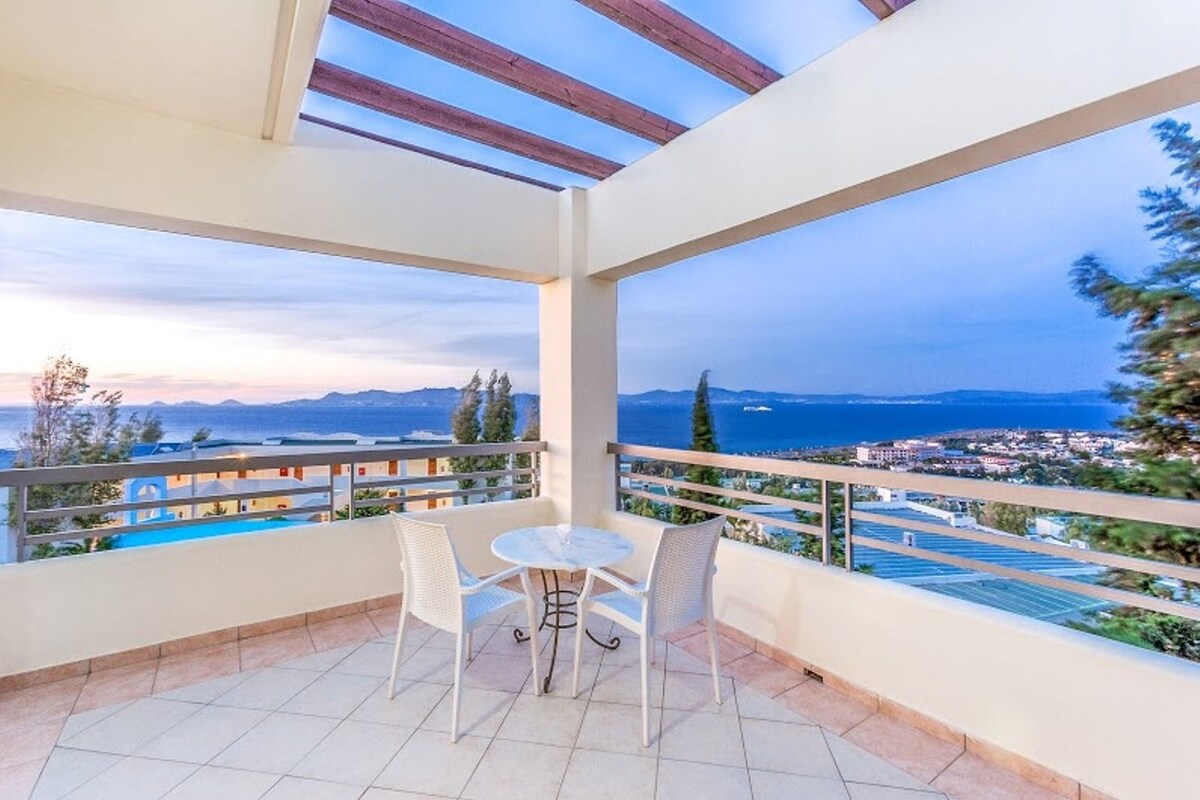 A balcony with a table and chairs, overlooking a coastal view with buildings and a body of water.