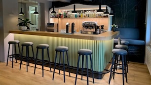 Un espace bar moderne doté d’un long comptoir, de nombreux tabourets, d’une machine à café et d’une variété de bouteilles.