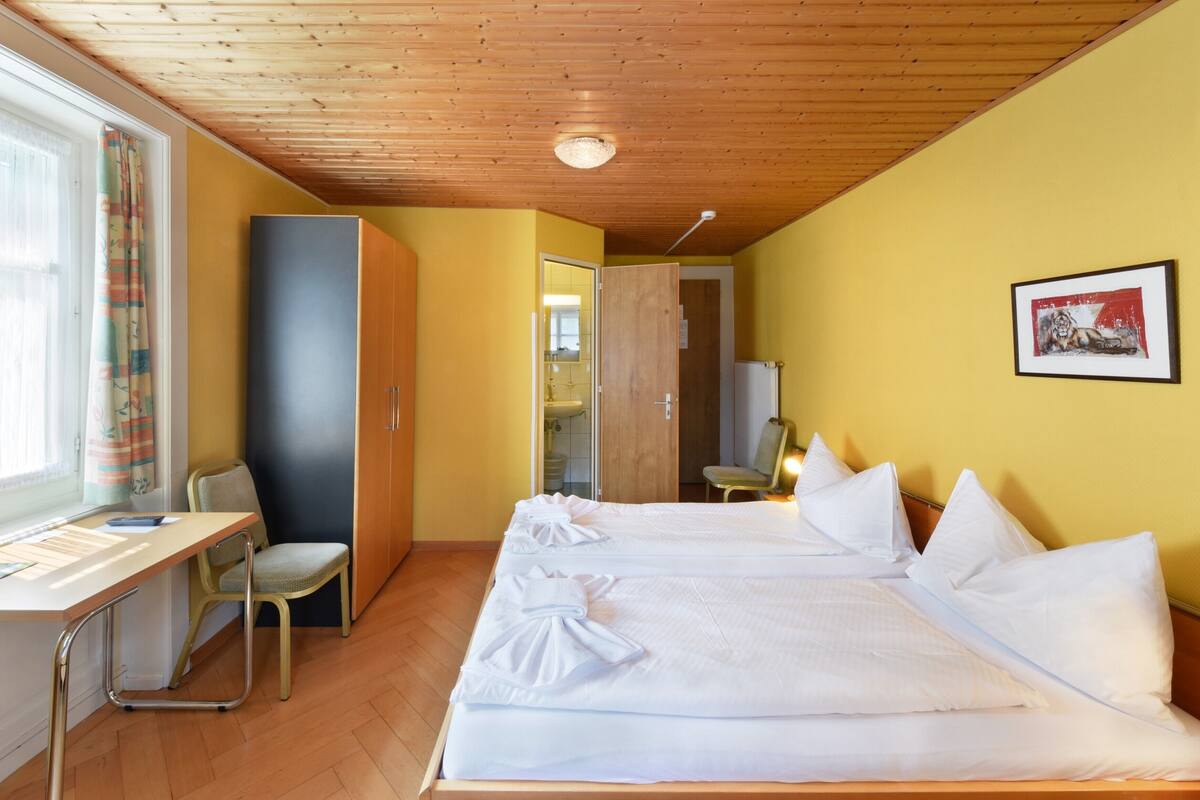 Une chambre d’hôtel avec deux lits, un bureau, une chaise et une armoire.