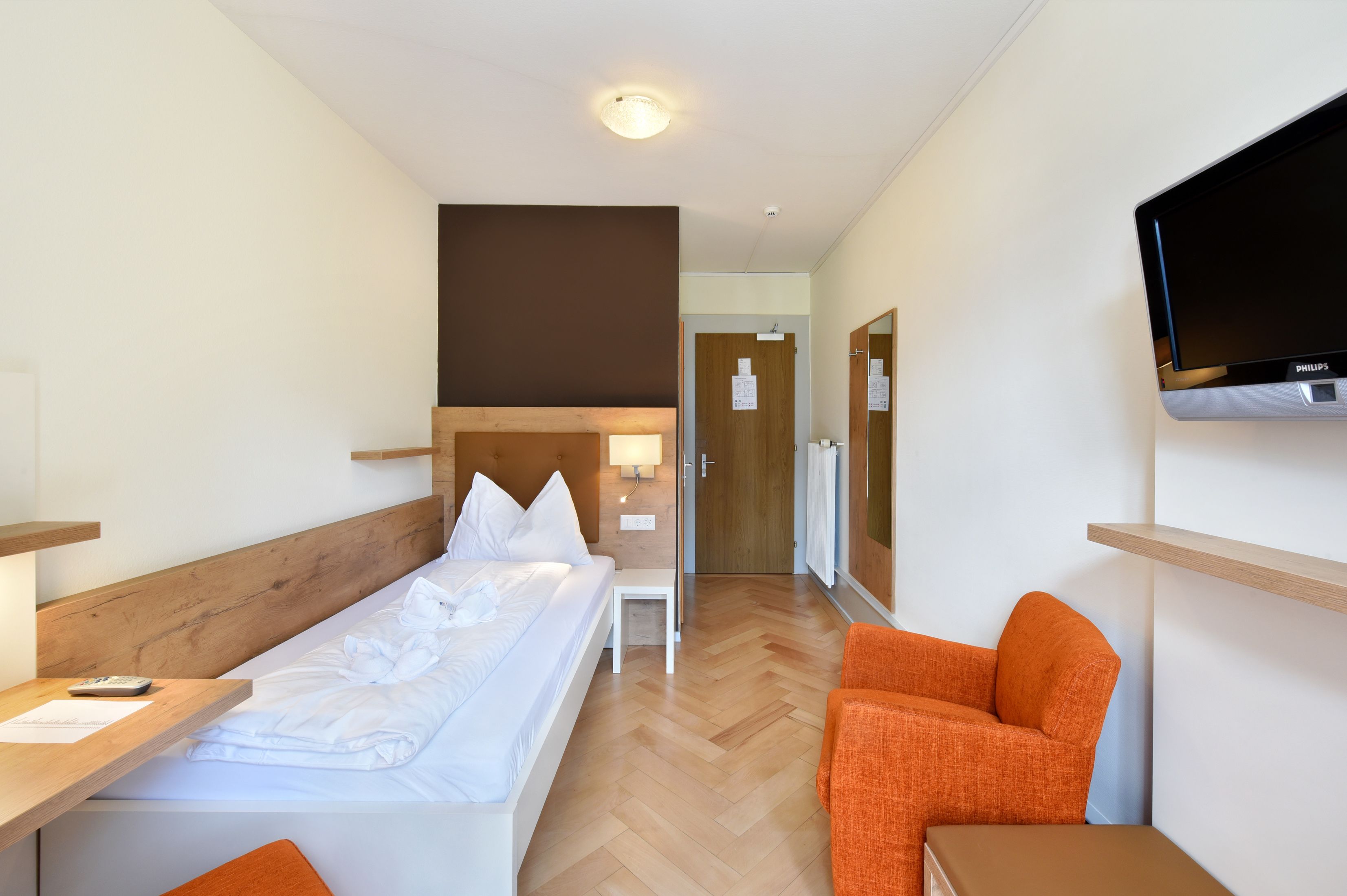 Ein Hotelzimmer mit Bett, Schreibtisch, Stuhl, Fernseher und einer Tür.