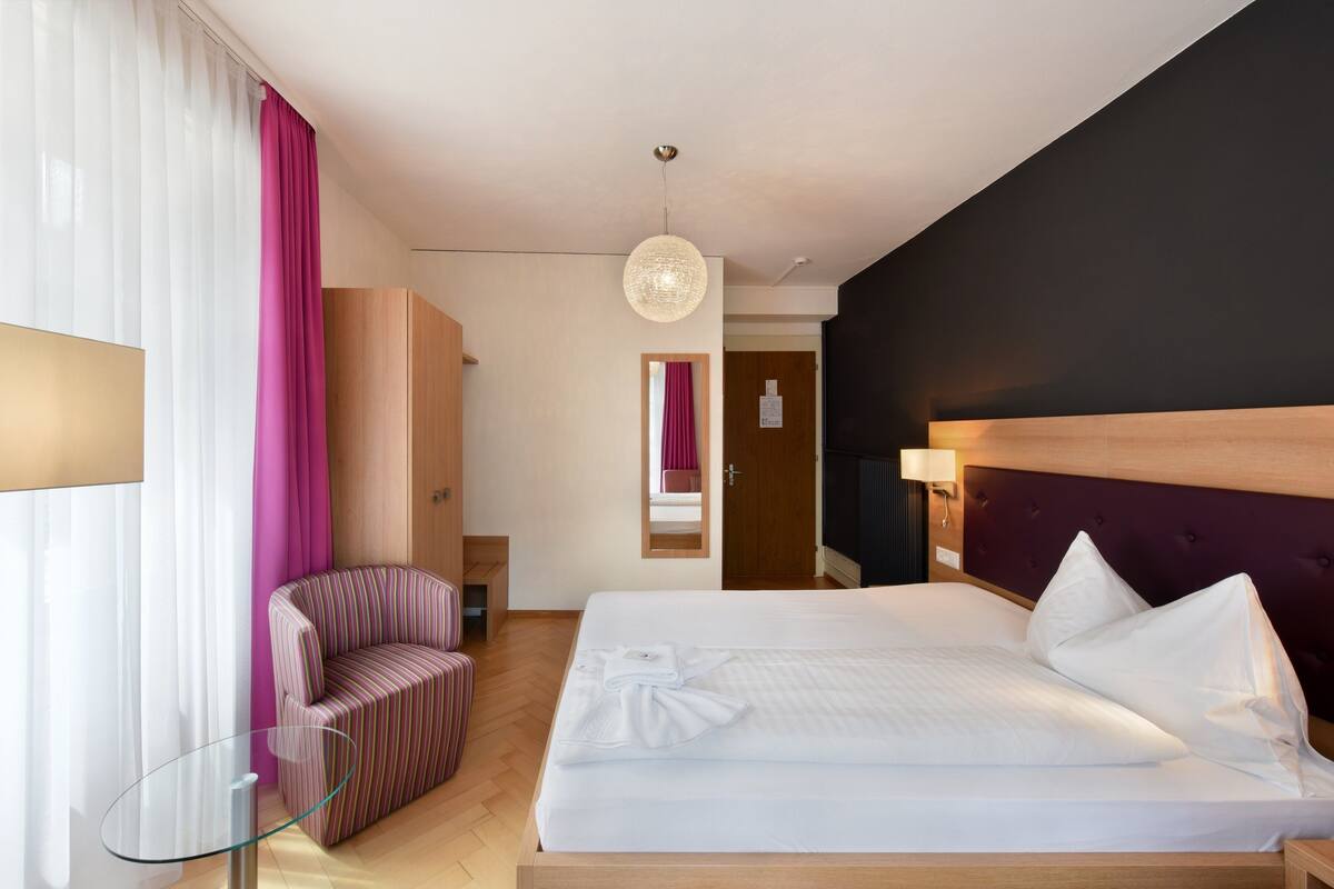 Une chambre d’hôtel avec un lit, une chaise, une table en verre et un miroir.
