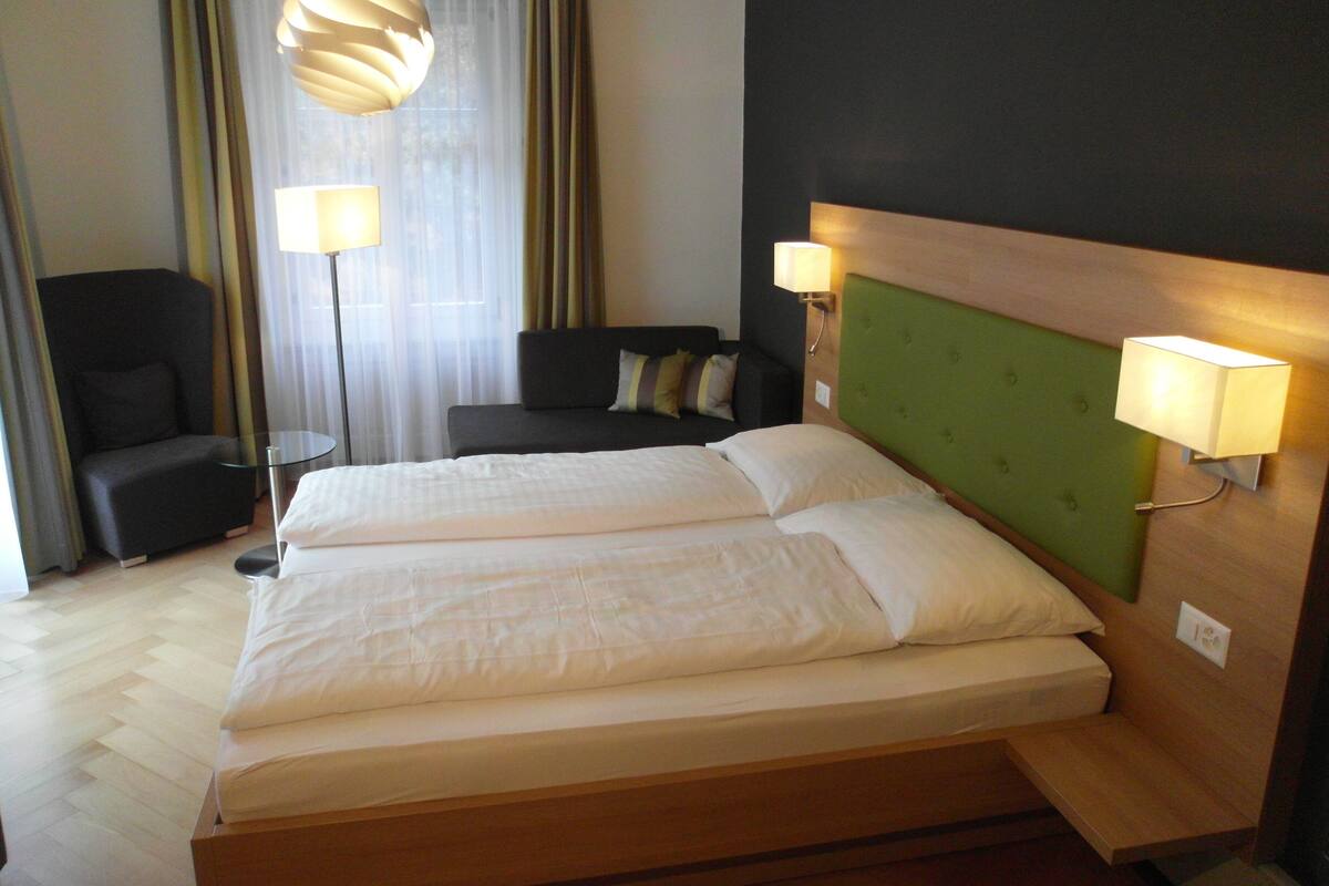 Une chambre d’hôtel avec un grand lit, une chaise, un canapé et deux lampadaires.