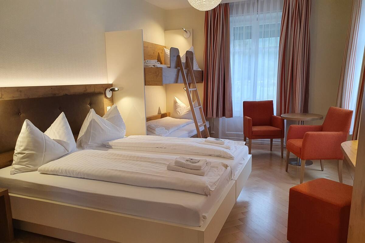 Une chambre d’hôtel avec un grand lit, deux chaises, une petite table et une échelle.