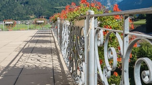 Un balcon doté de rampes en métal et orné de fleurs rouges, offrant une vue sur un paysage montagneux aux sommets enneigés.