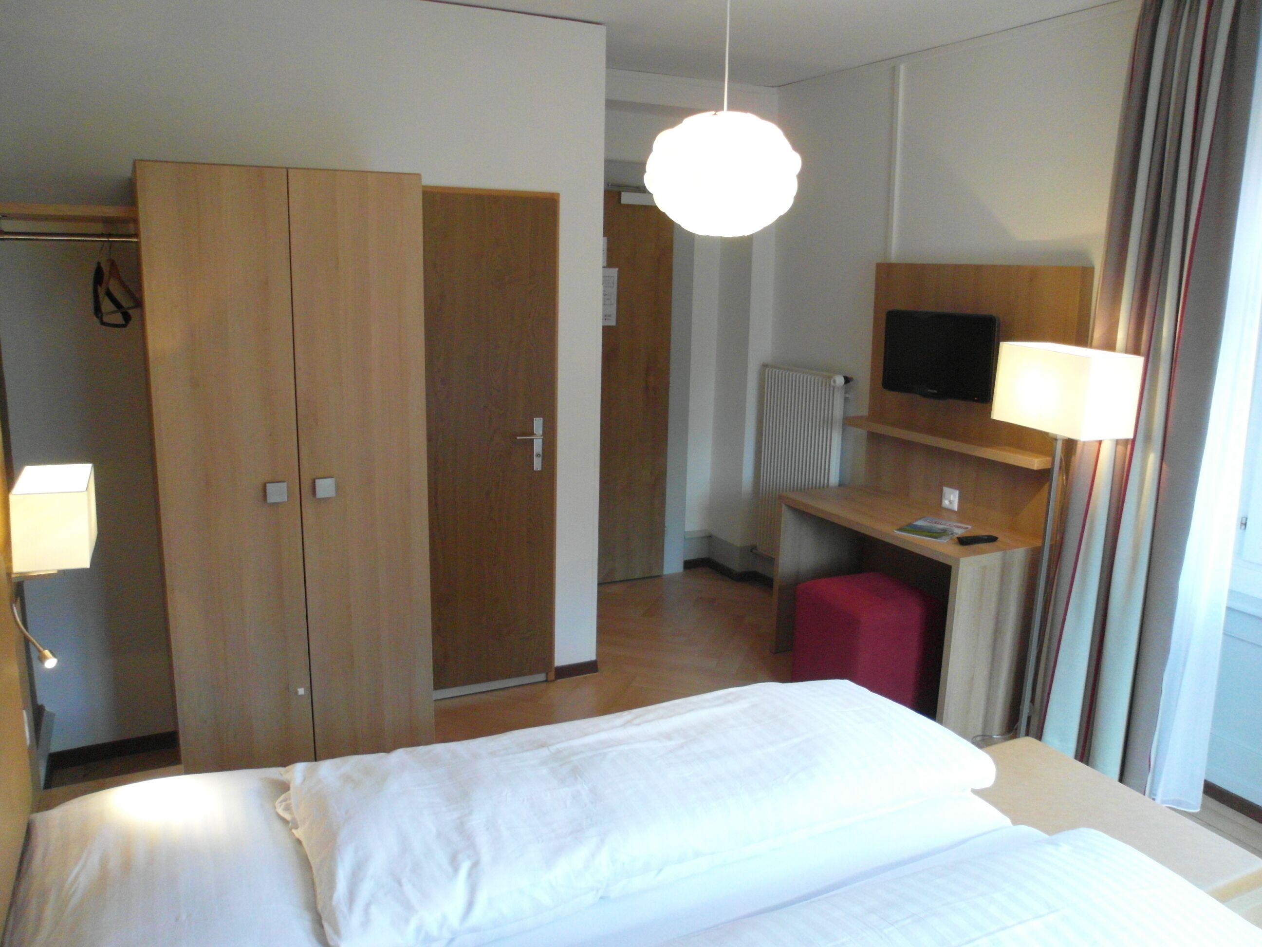 Ein Hotelzimmer mit einem Bett, einem Schreibtisch mit Stuhl, einem Fernseher und einem Kleiderschrank.