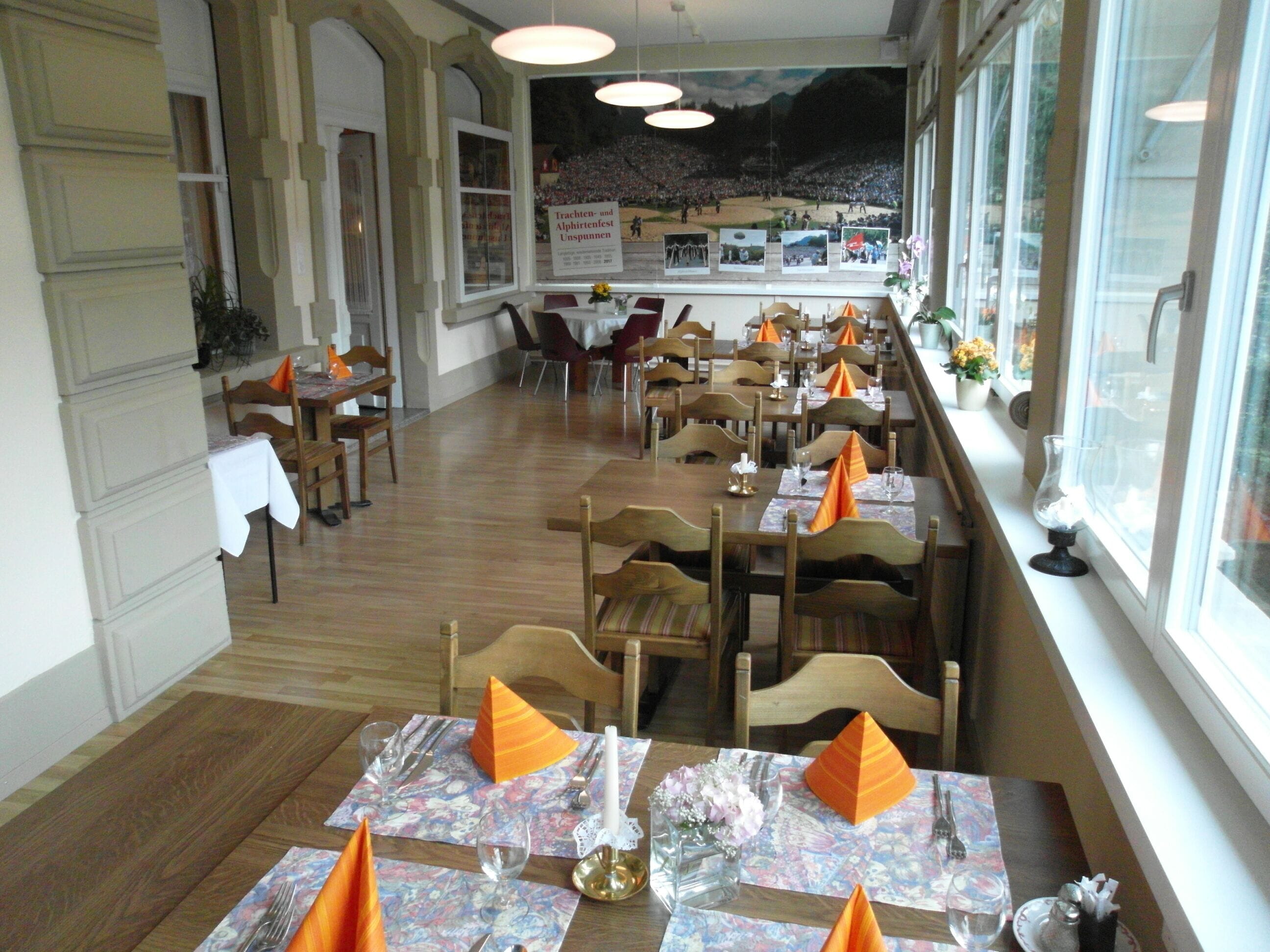 Un espace repas avec des tables dressées pour le service, des chaises et une vue sur un événement en plein air grâce à de grandes fenêtres.