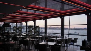 Un restaurante con mesas y sillas, ventanas amplias y vista al agua.
