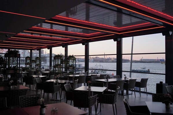 A restaurant with tables and chairs, large windows, and a view of the water. - Delta 4 (Tulcea)
