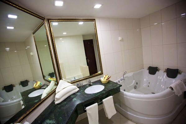 Un baño con un espejo grande, dos lavamanos, una bañera y toallas.