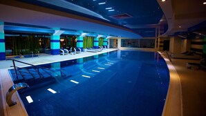 Una piscina interior de diseño curvo, con varias pistas de natación y un área de descanso con sillas y una pequeña mesa.
