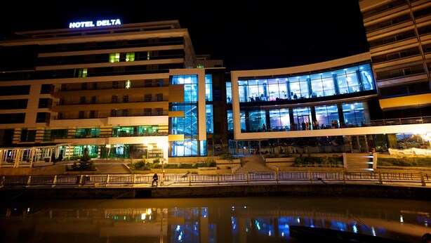 Un hotel moderno con un llamativo letrero que dice 'HOTEL DELTA', fachada de vidrio y ubicación frente al agua.