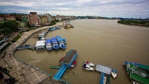 A riverfront with boats docked, a pedestrian walkway, and buildings in the background.